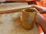 Handwerk: Kind formt und bemalt einen kleinen Tongefäßbecher mit Herzmotiv.