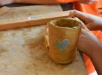 Handwerk: Kind formt und bemalt einen kleinen Tongefäßbecher mit Herzmotiv.